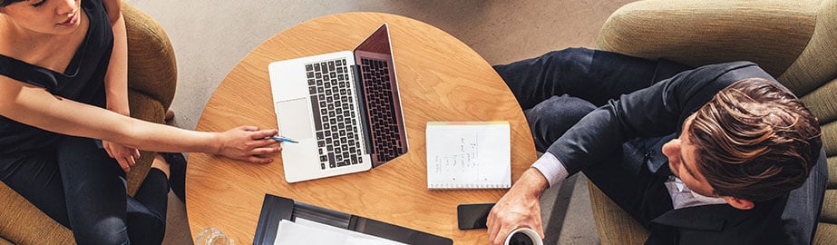 Colleagues review notes together with laptop and coffee.