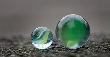 Image of two green marbles, one large and one smaller, on a concrete surface