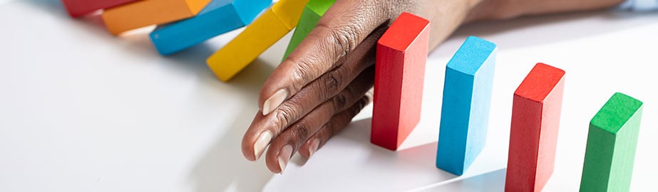 Photo of a hand stopping colorful dominos from falling