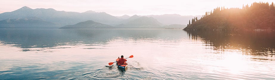 Kayaker on lake in early morning with mountains in background