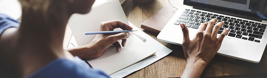 Woman types on laptop with pencil in hand