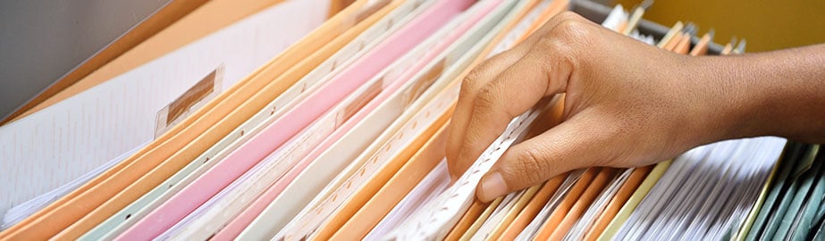 Close up of person looking through filing cabinet and pulling out piece of paper