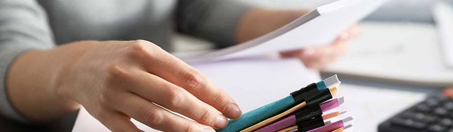 Office worker looks at stack of papers bound with paperclips